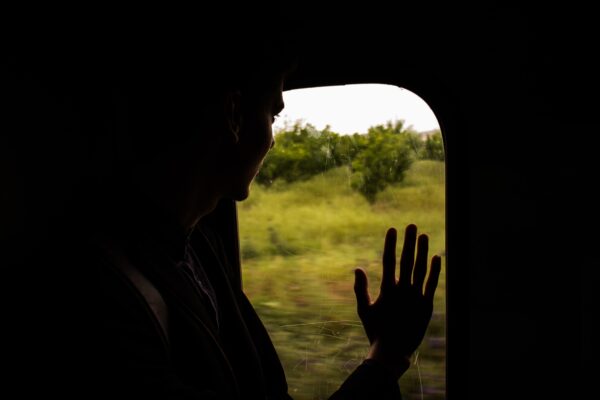 Ragazzo meridionale guarda fuori dal finestrino del treno e con la mano saluta qualcuno.